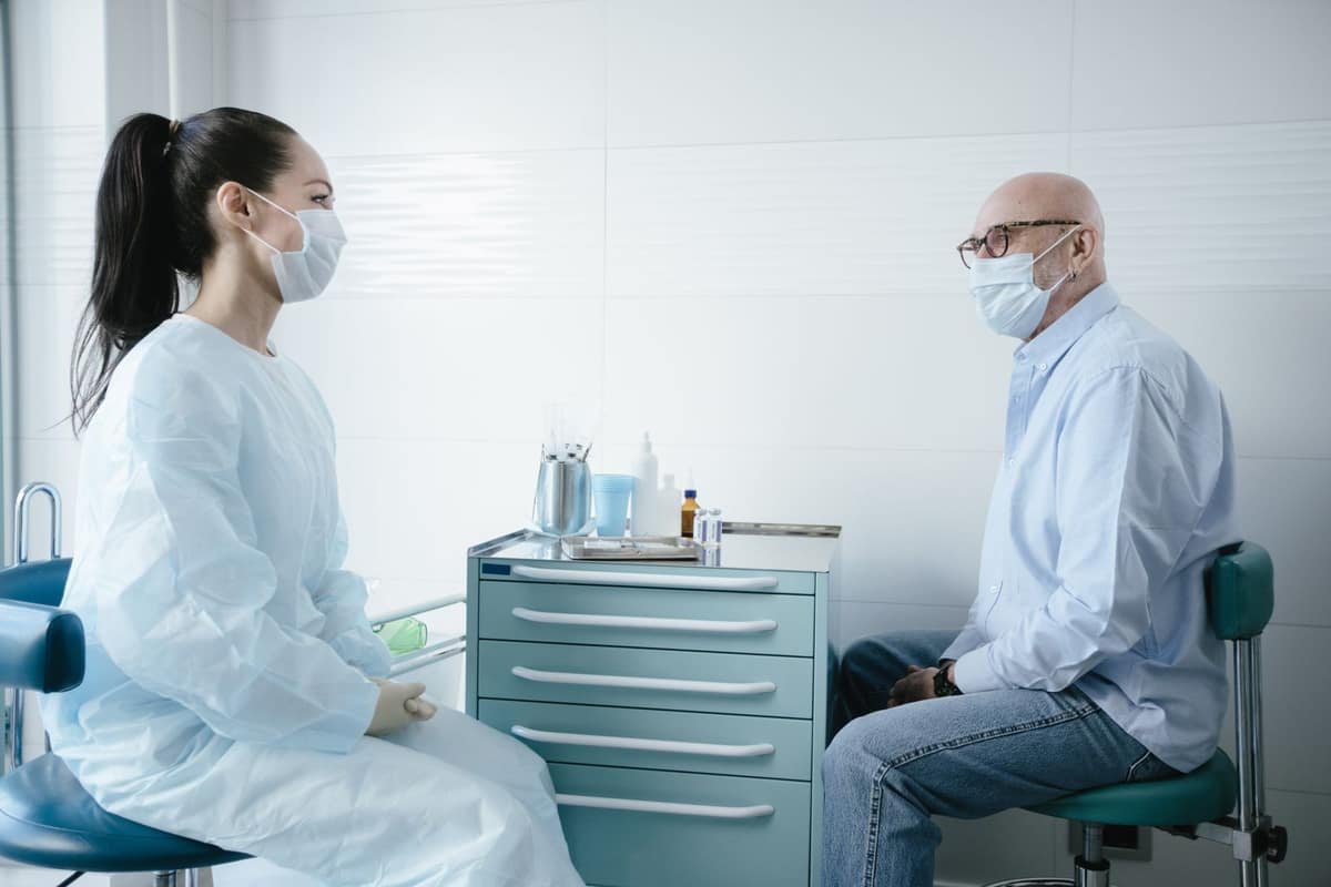 Older patient in a light shirt speaking with a healthcare professional in a bright clinic examination room